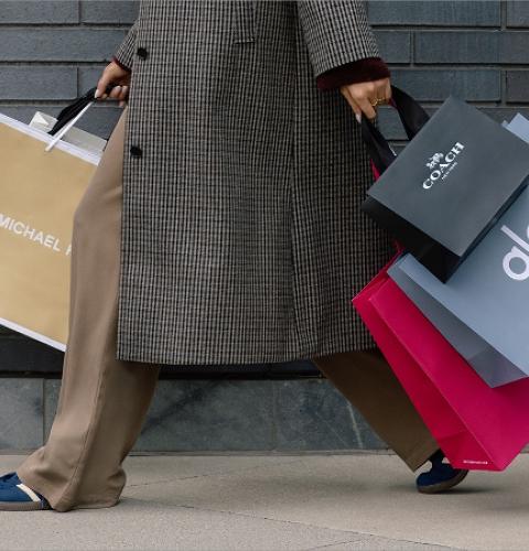 Shopper holding Michael Kors, Coach and Alo bags against a brick wall