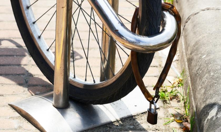 Bicycle locked to a metal rack on a brick sidewalk in sunlight