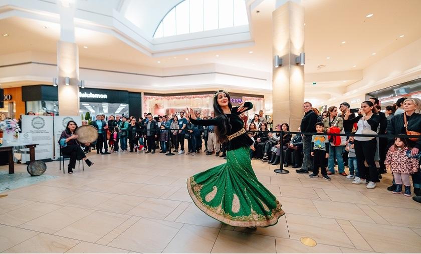 Dancer in a green skirt performing for a crowd in a mall atrium