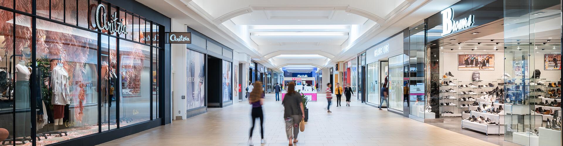 Shoppers walking through a bright mall concourse past Aritzia and Browns stores