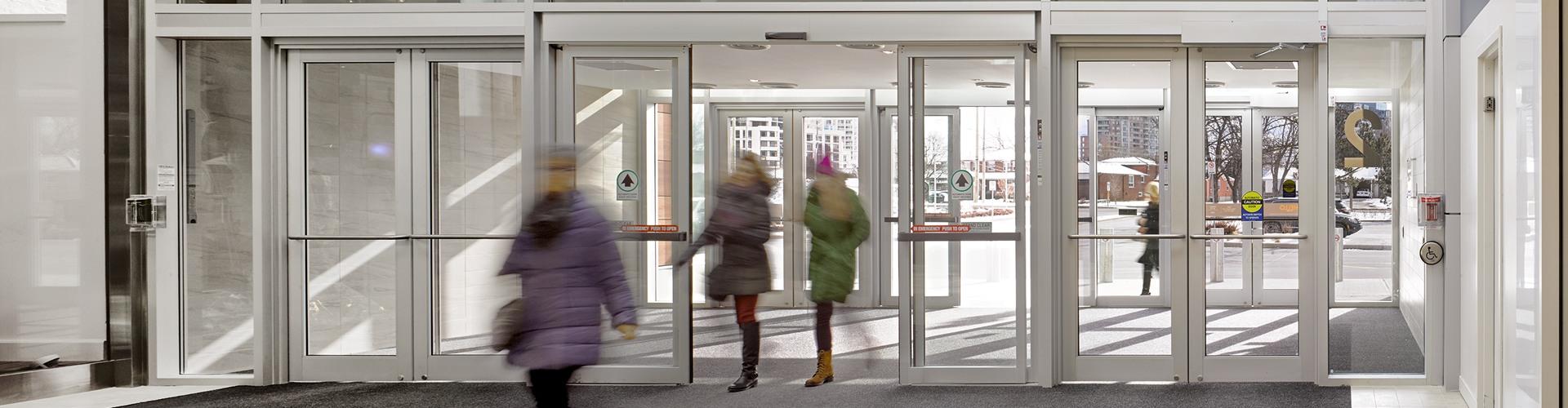 Shoppers in winter coats entering a mall through glass sliding doors
