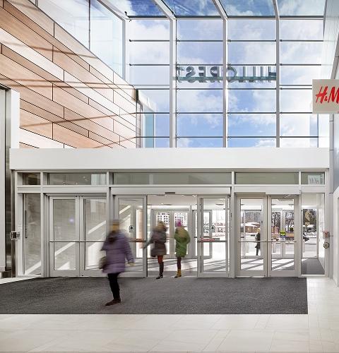 Shoppers in winter coats entering a mall through glass sliding doors