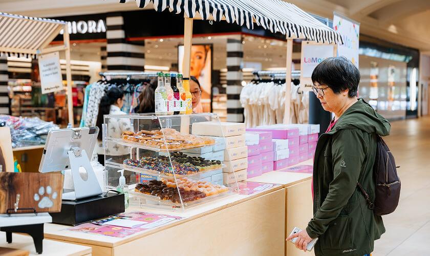 Woman browsing a mall doughnut pop-up stall with glass display cases