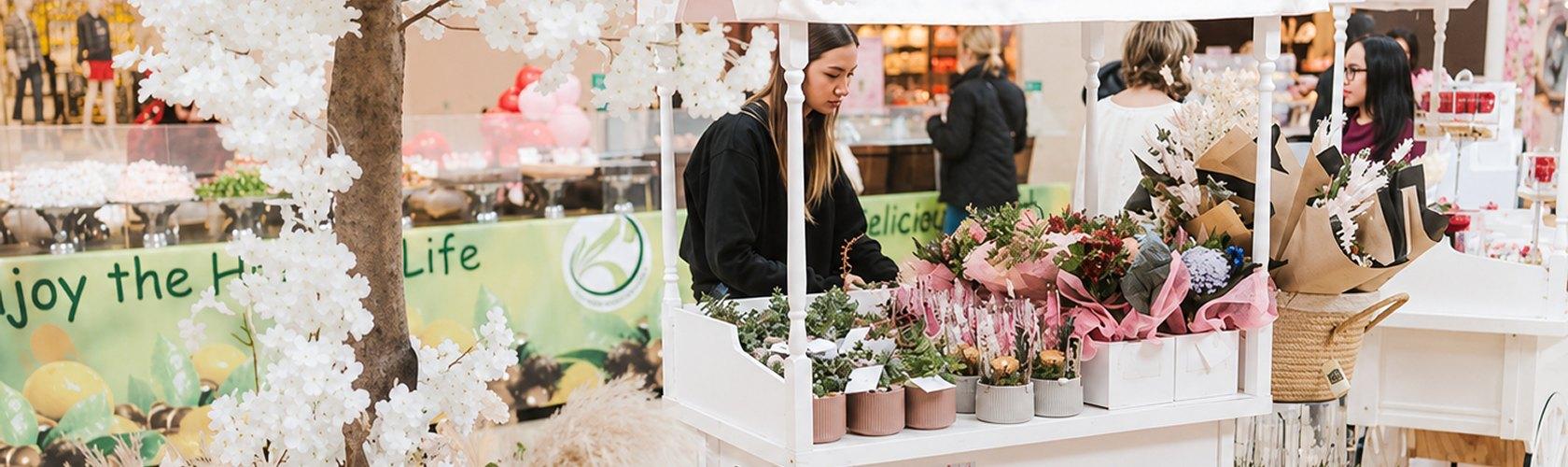 Woman arranging bouquets at a white mall flower cart with blossom tree