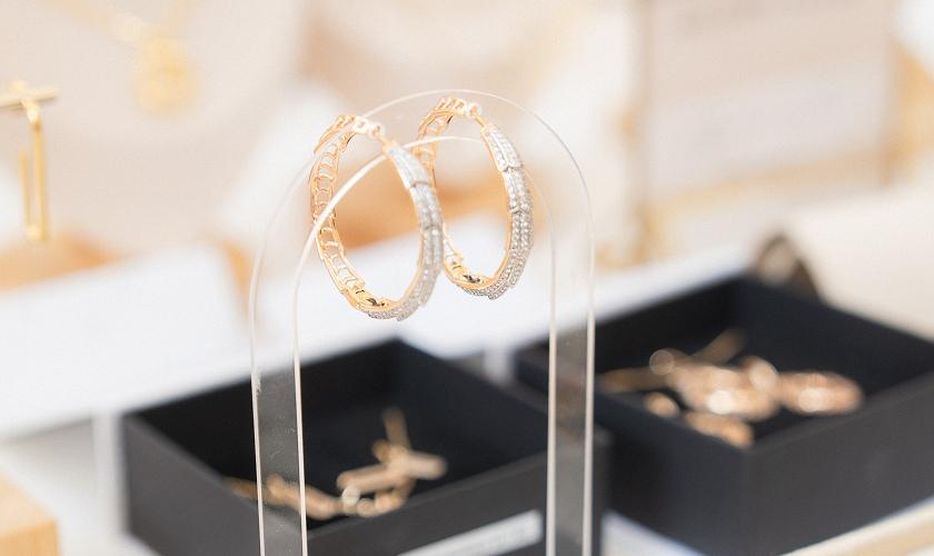Gold and crystal hoop earrings displayed on a clear jewellery stand