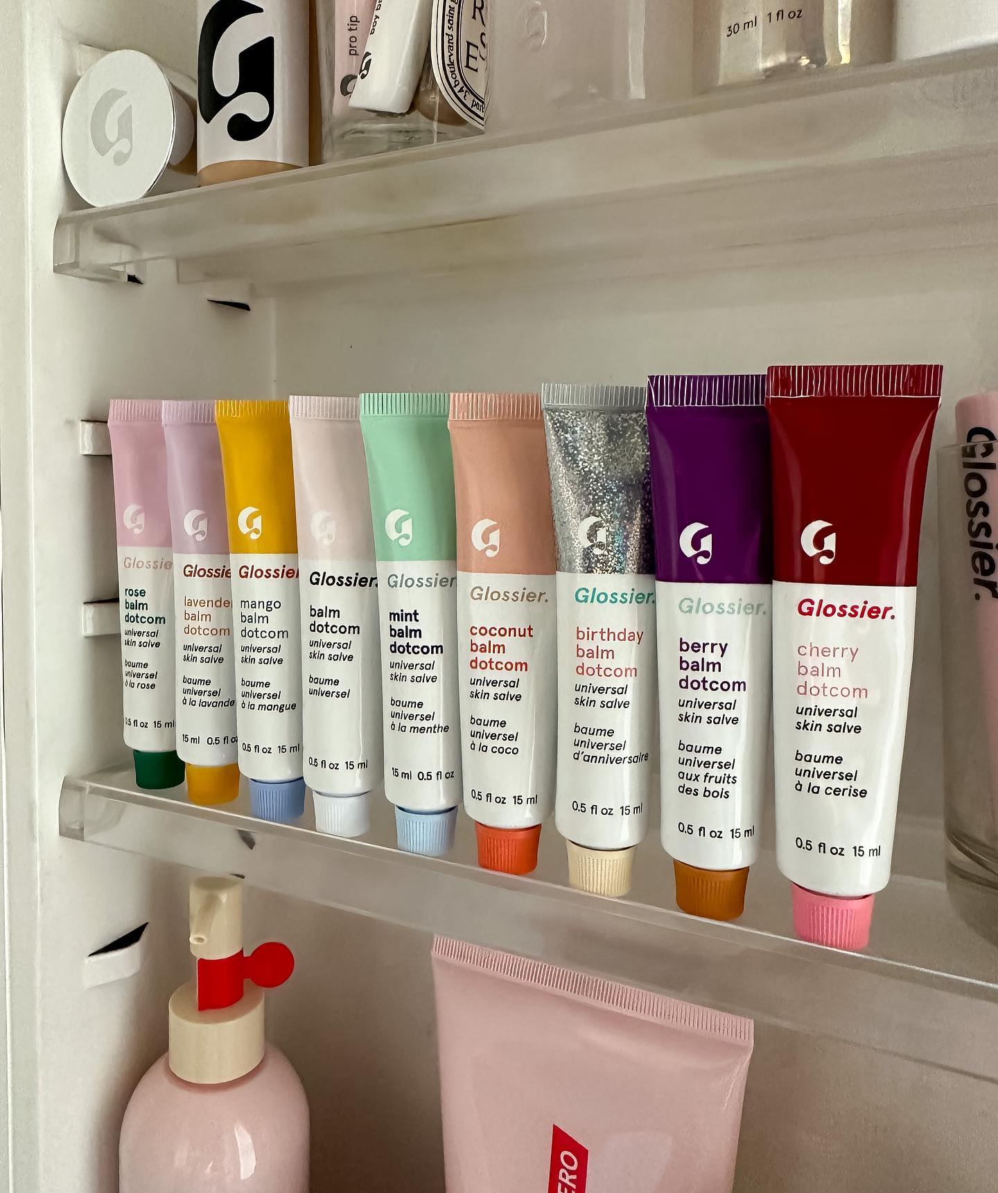 Various shades of Glossier's lipgloss are on display in a bathroom cabinet.