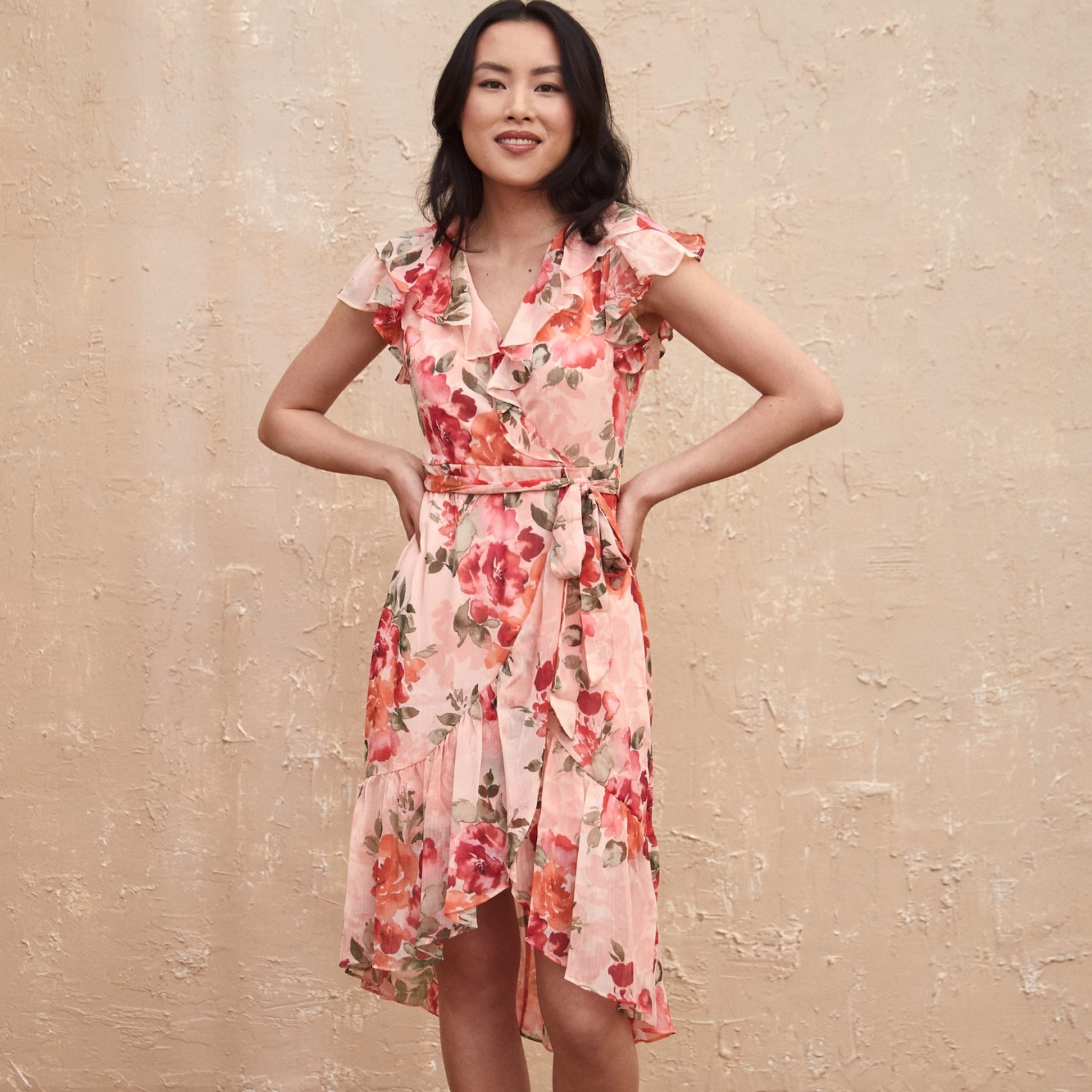 A dark haired woman is wearing a floral, light pink dress from Laura.