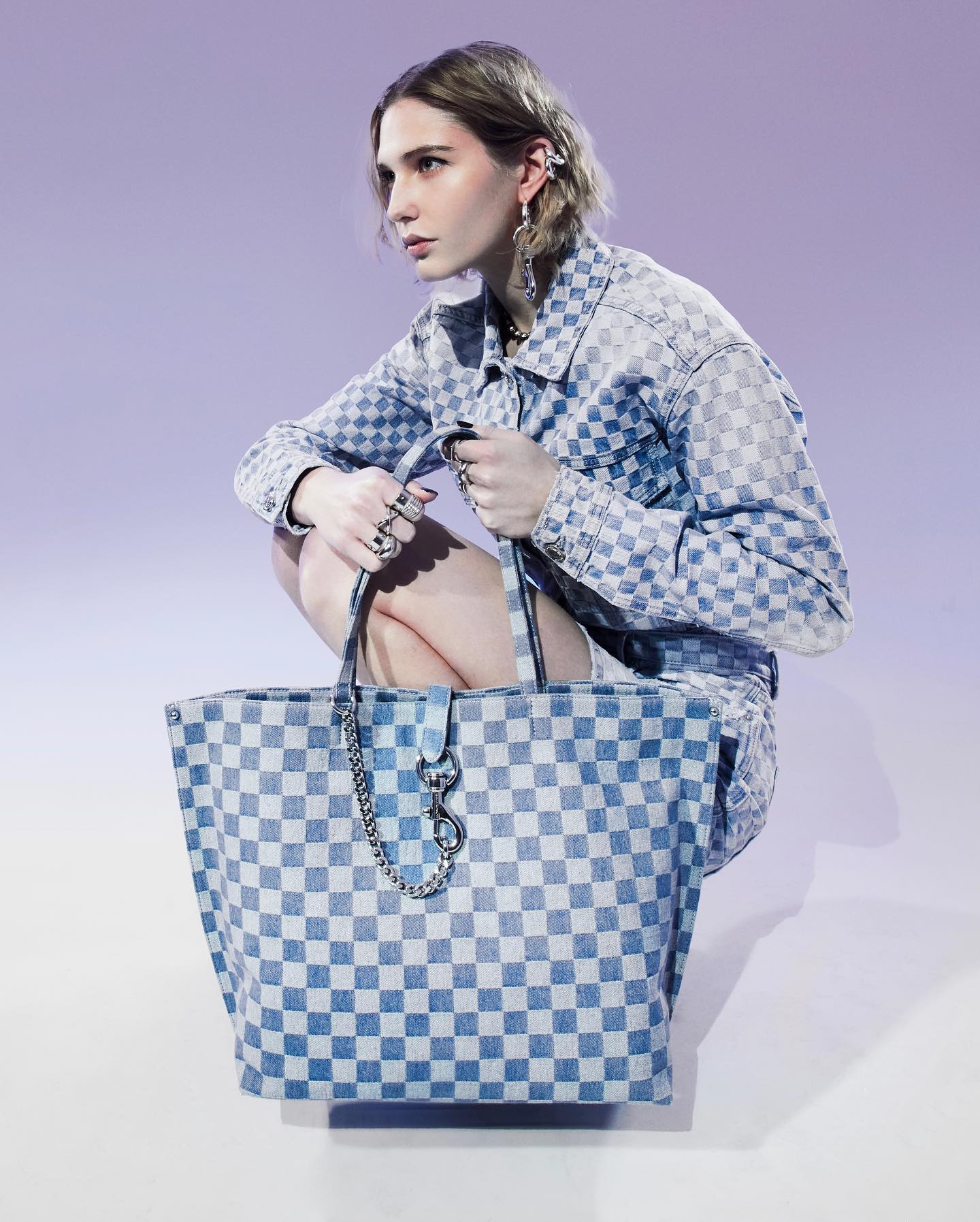 A woman is bending down and holding a blue checkered purse from Rebecca Minkoff. Her jacket matches the bag.