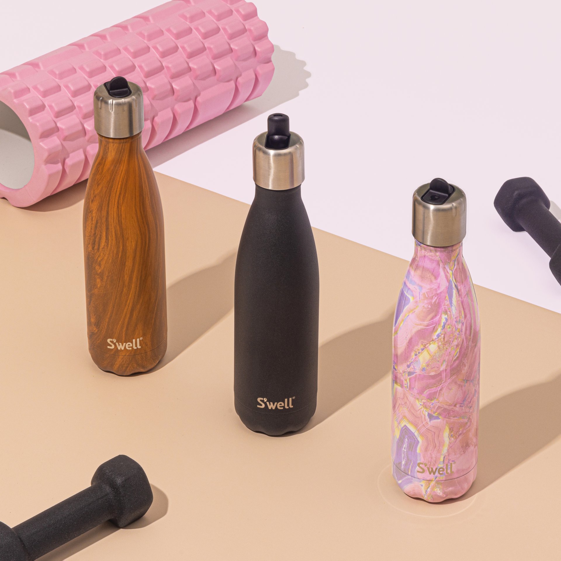 Three S'Well water bottles of different designs are positioned alongside workout equipment.