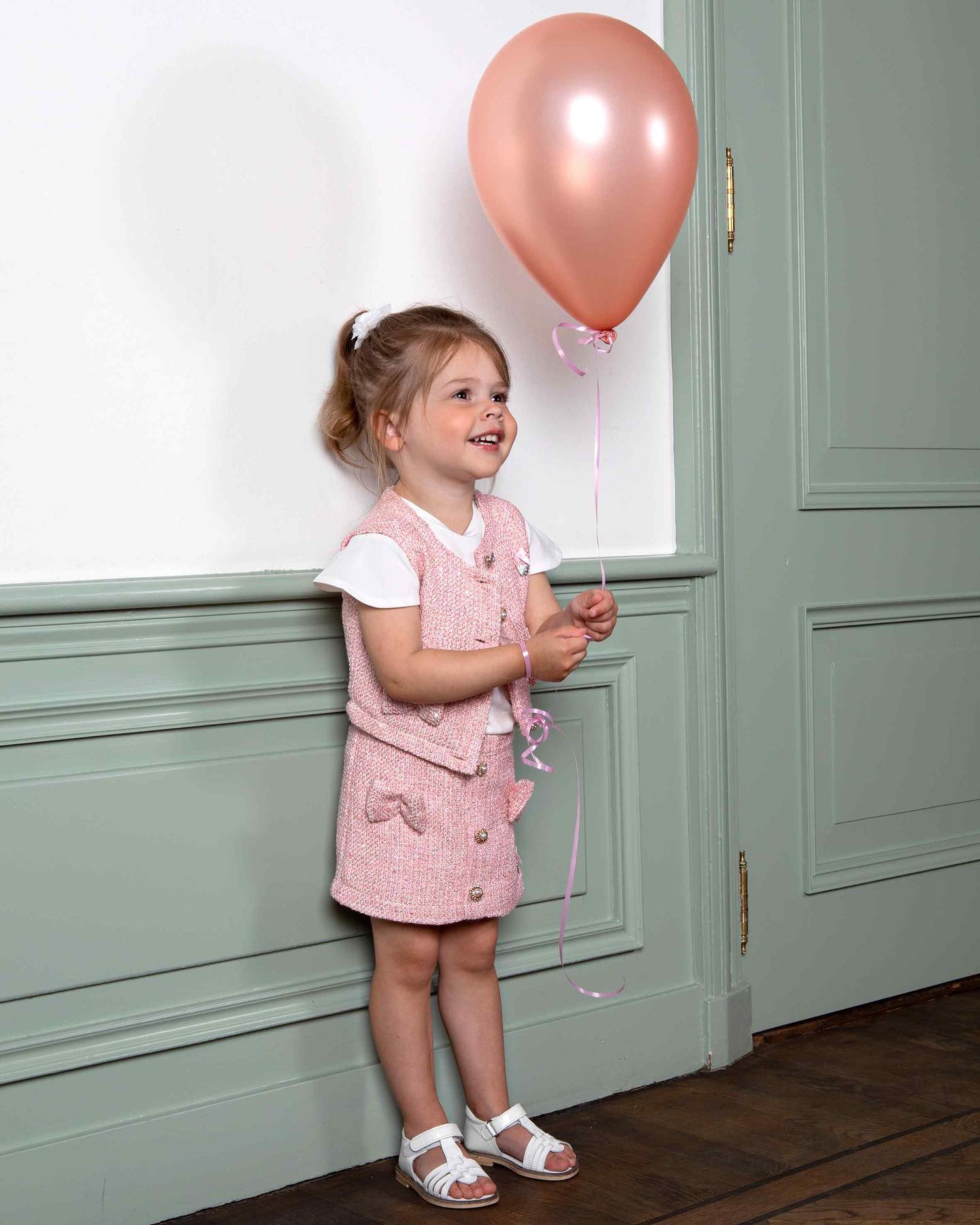 A young girl in a pink dress from Hunter & Shaye holding a pink balloon.