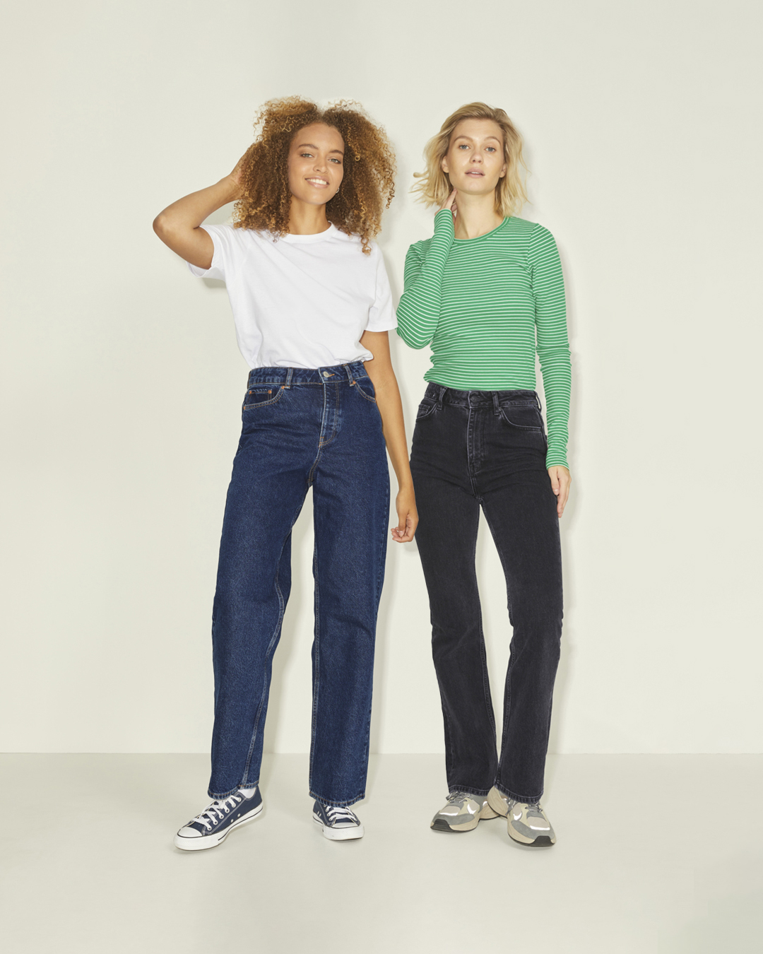 Two women show off their outfits from Hudson's Bay. One woman wears a white shirt and jeans. The other woman wears a green long sleeve and black jeans.
