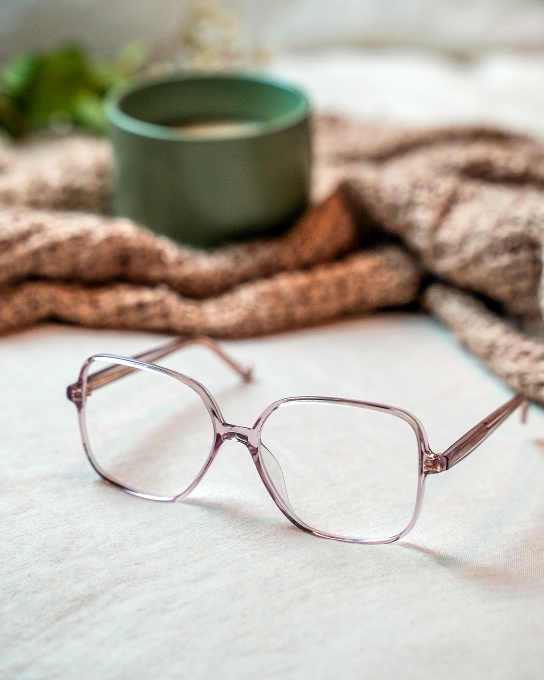 A pair of glasses from Specsavers are laid out beside a blanket and cup of coffee.