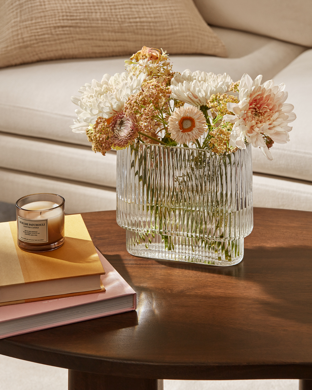 A ribbed glass vase sits on a coffee table. The vase is filled with lowers.