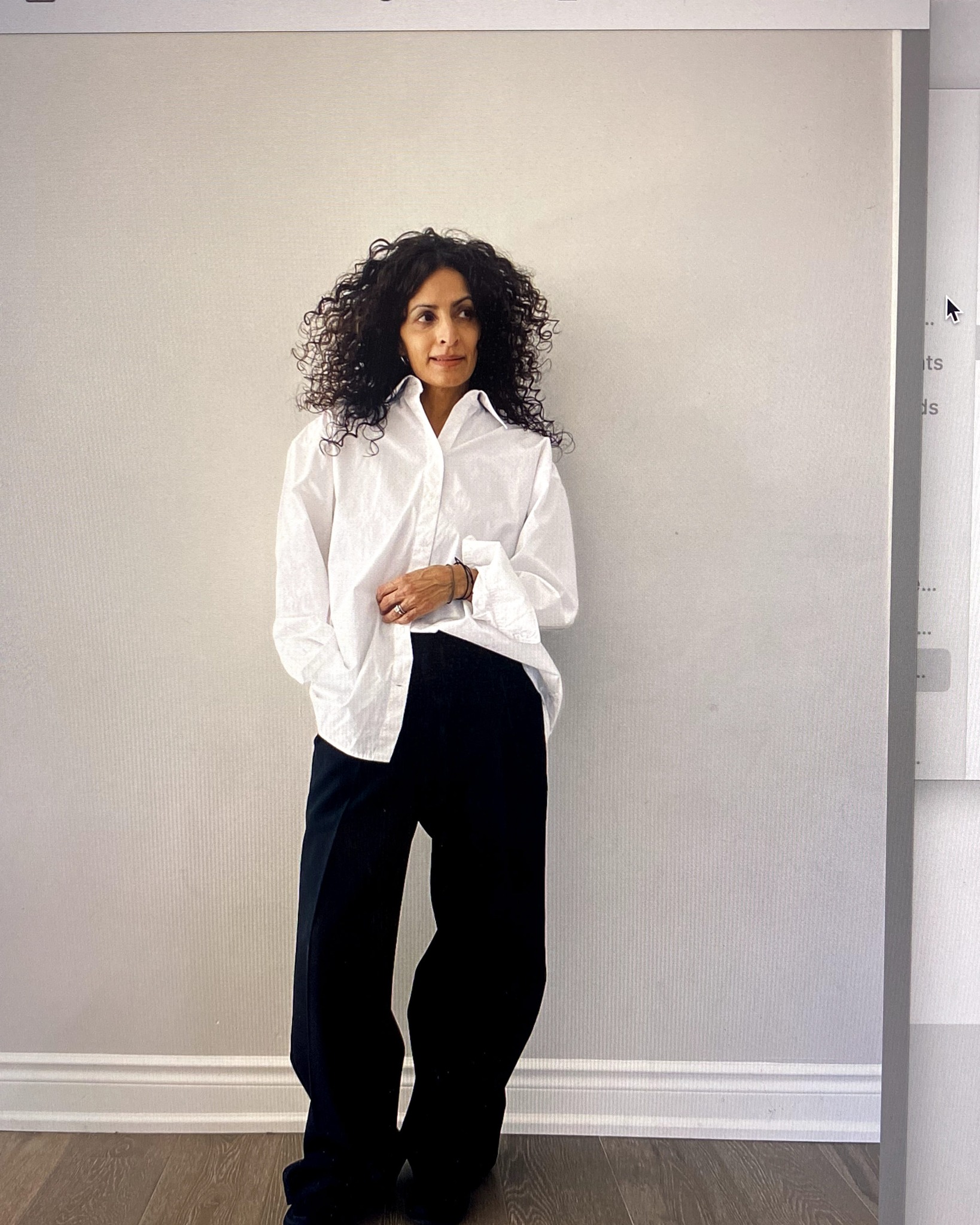 A woman stands against a wall wearing a white button down and black pants from Aritzia.