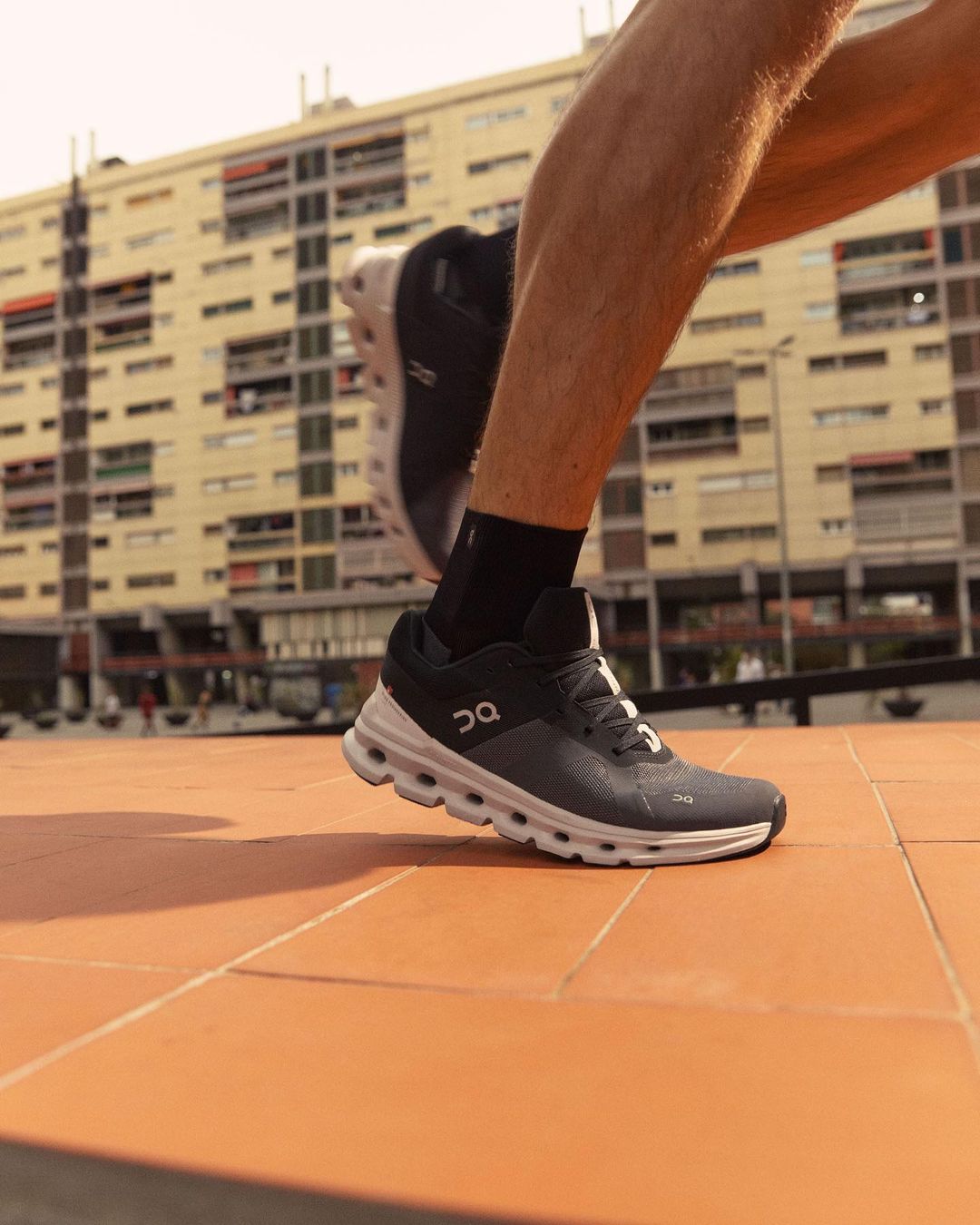 A close up shot of a man running on a track. He is wearing black and white sneakers and black ankle socks