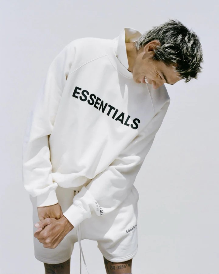 mid close-up image of a man wearing a white essentials hoodie and matching white shorts