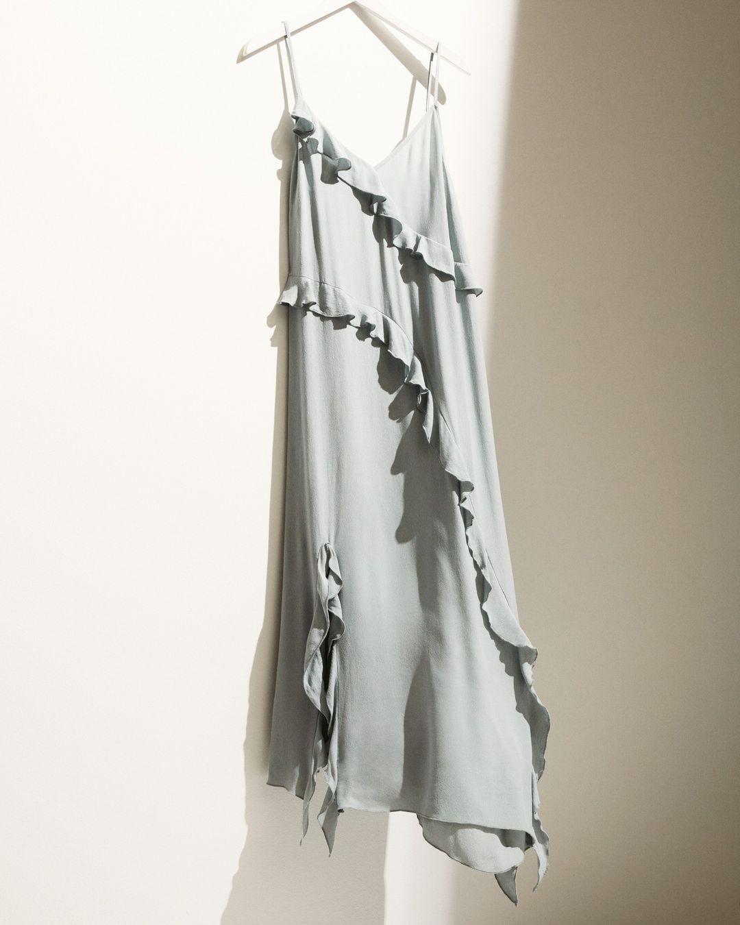 image of a seafoam green H&M dress with ruffles and an asymmetrical hem hanging on a hanger against a white wall