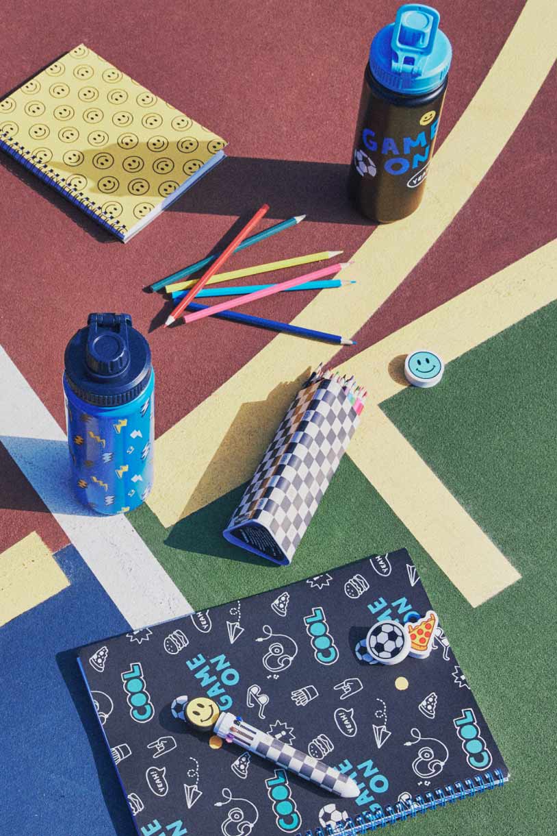 flat lay stylized image of school supplies on a track, including water bottles, notebooks, pencils and a pencil case