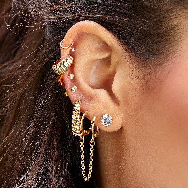 Woman's ear with multiple piercings and gold earrings.