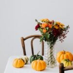Table with white tablecloth. Pumpkins and vase with flowers on top as decor.