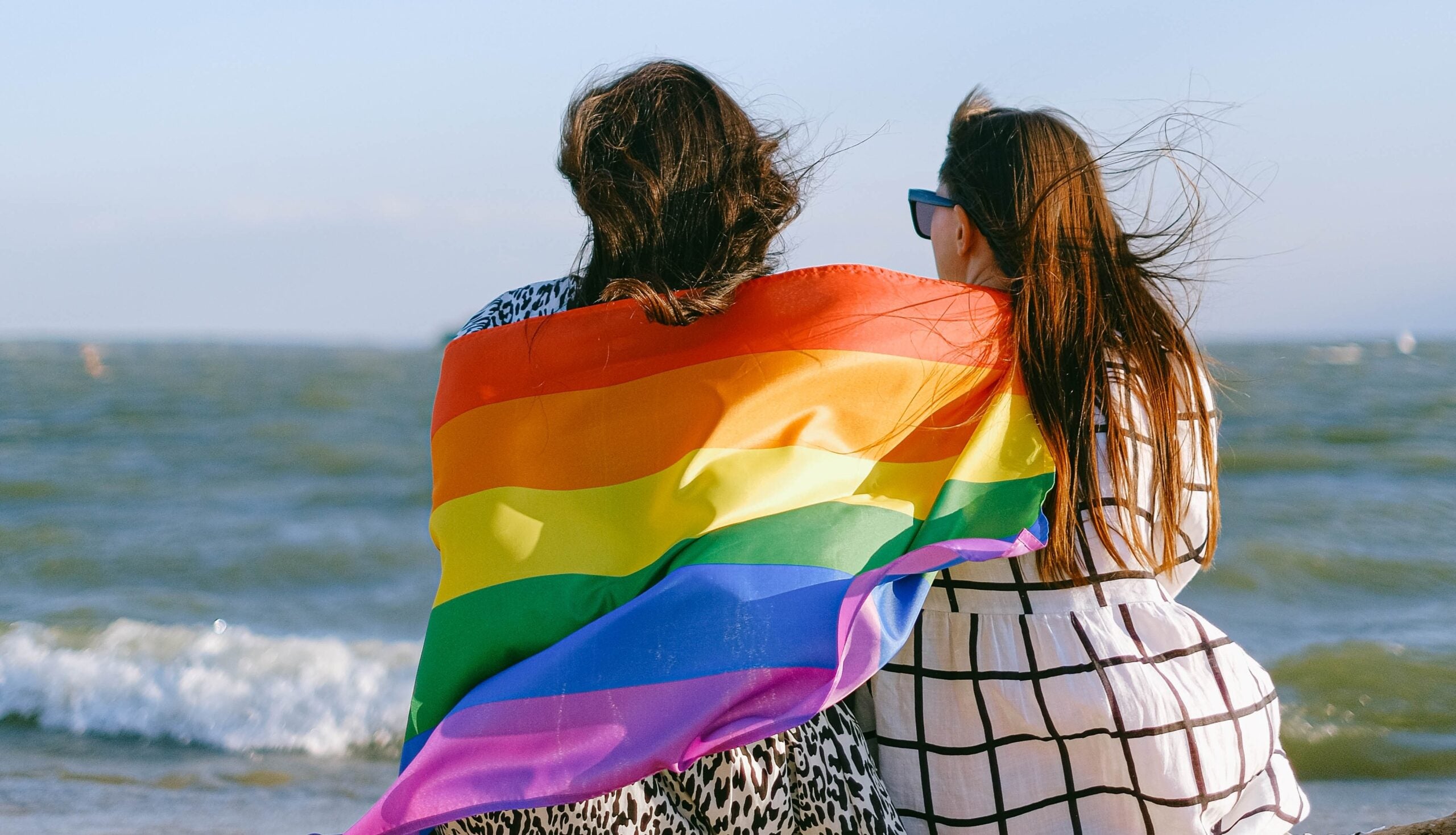 Couple sitting on the beach with Pride flag wrapped around them