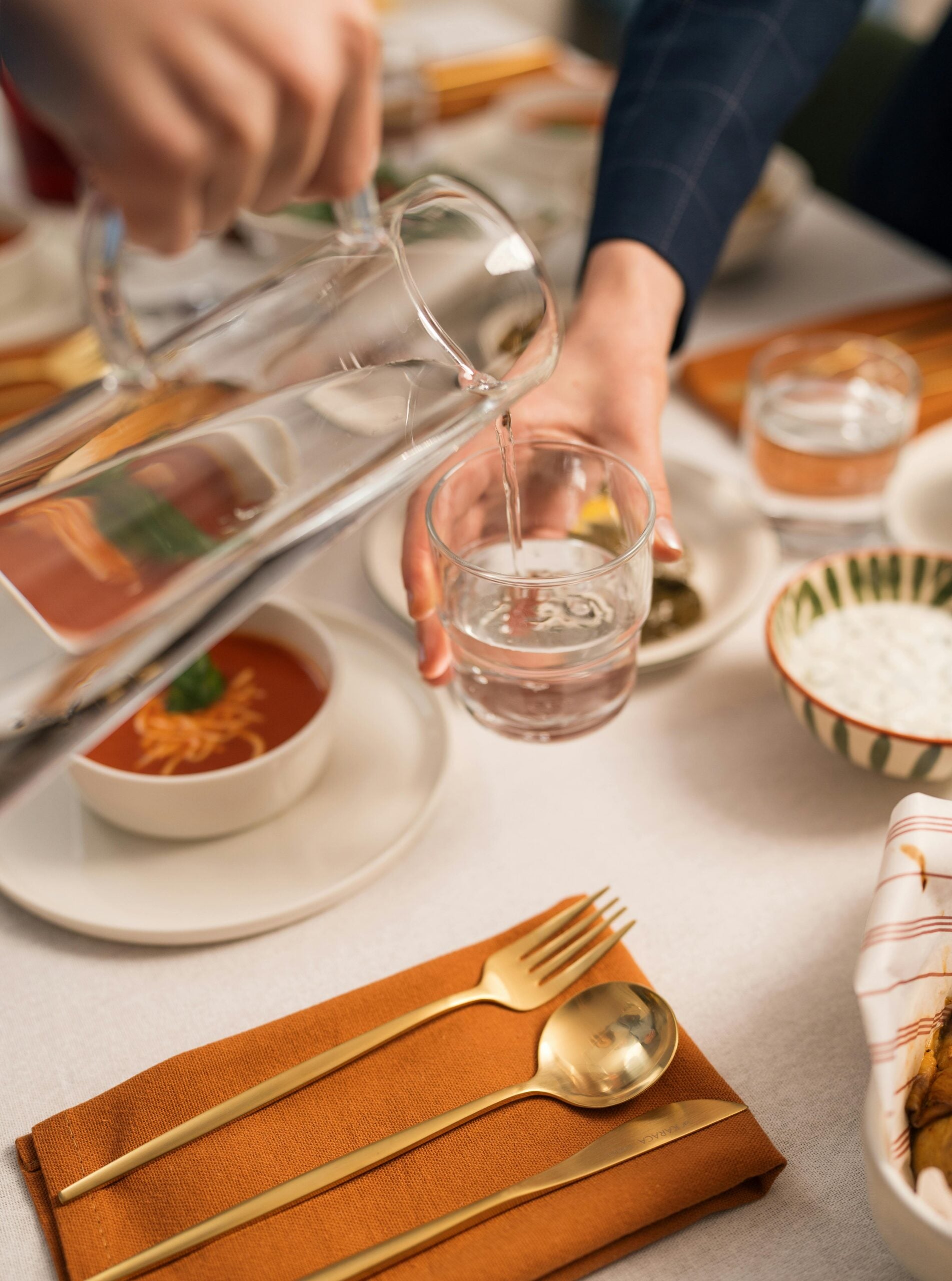 person pouring water into glass over tablescape