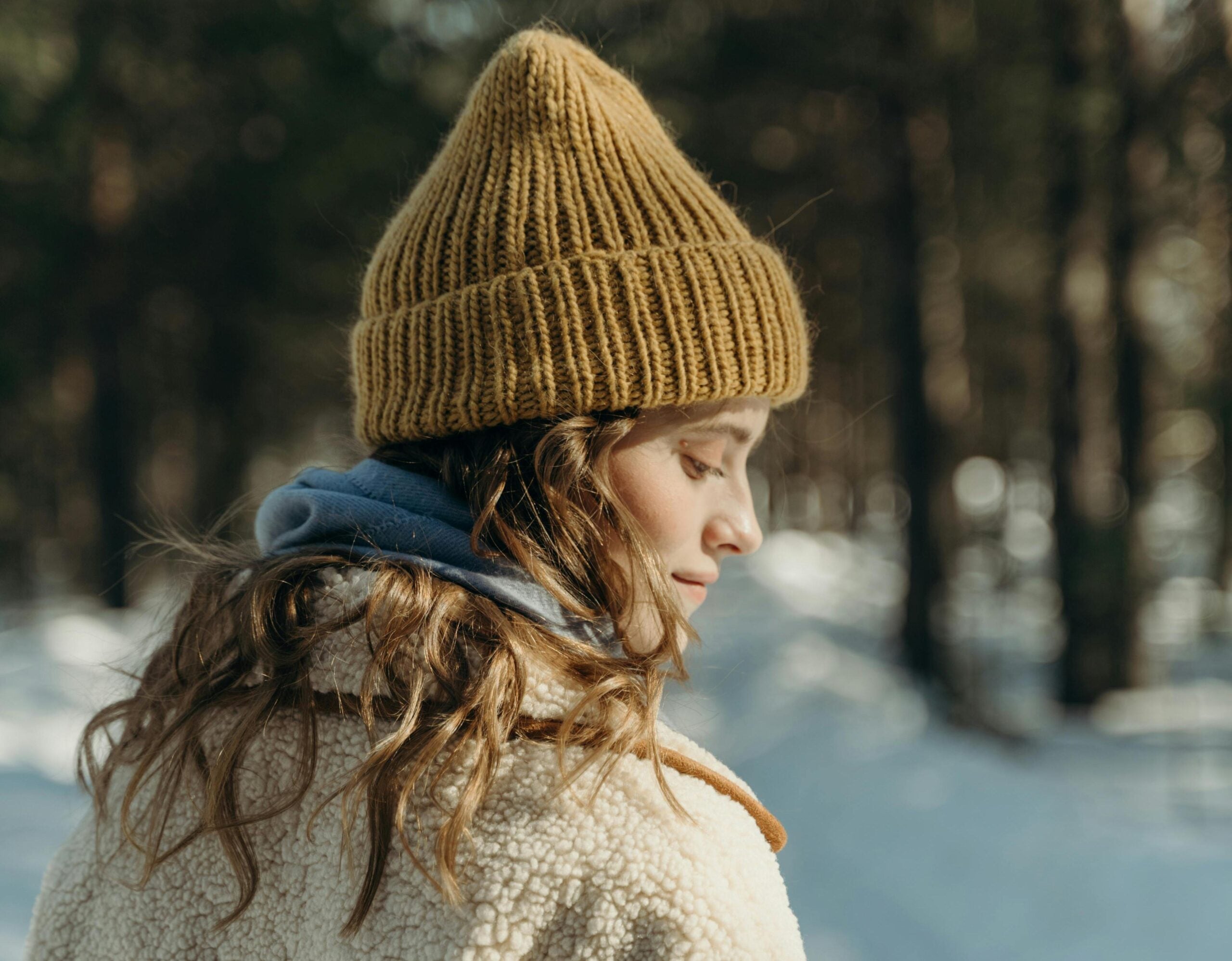 Woman in the forest with a cream jacket, Blue Scarf and Brown Hat.