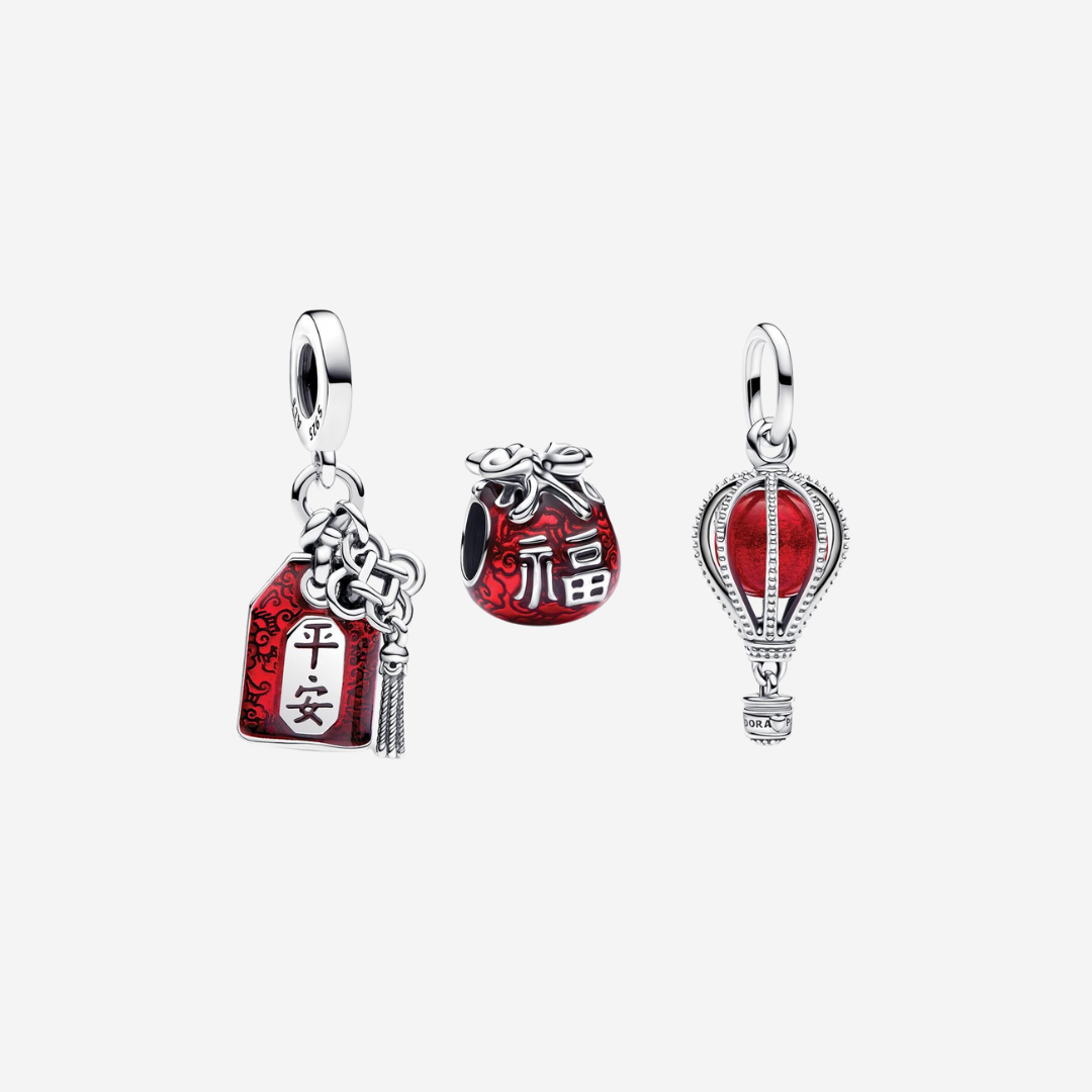 The set includes the Lucky Bag Charm, a sterling silver pouch adorned with red enamel and the Chinese character Fu, symbolising happiness and prosperity. The Lucky Amulet Double Dangle Charm features a red envelope design with auspicious cloud patterns and the word 平安 (ping'an), meaning “peace.” Completing the trio, the Hot Air Balloon Murano Glass Dangle Charm is crafted in sterling silver and features a red Murano glass balloon, symbolising new journeys and inspiration.